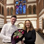 Eine Frau und ein Mann tauschen lächelnd in einer Kirche einen Blumenstrauß aus.