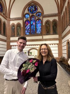 Eine Frau und ein Mann tauschen lächelnd in einer Kirche einen Blumenstrauß aus.