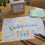 Zeichnung "Kinderparlament" auf Tisch, mit Malstiften und ähnlichem
