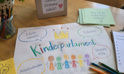 Zeichnung "Kinderparlament" auf Tisch, mit Malstiften und ähnlichem
